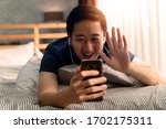 Portrait of happy 30s aged Asian man making facetime video calling with smartphone at home. He's waving on phone screen. Using conferencing meeting online app, social distancing, concept