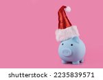 Piggy bank in a Christmas red cap against the pink background 