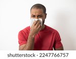 Small photo of photo of young dark-skinned, ill, student, worker patient with allergy, cold blowing nose with right hand, kleenex, looking miserable, isolated on white background. fever, vaccination