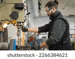 A man in protective clothing who works in a metalworking company is making a hole for a job using a bench drill, or press drill, milling machine. Industrial manufacturing concept.