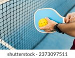 A close-up of a hand of an athlete with a pickleball racket and a ball about to make a serve. Pickle ball concept. Sports that are played with rackets.