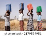 Four very young African girls marching in a line with colored canisters on their heads, sympolising that fetching water is a woman's job, regardless of age