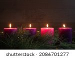 Advent wreath with all four pillar candles lit for fourth week of advent with evergreens boughs and wood background with copy space