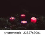 Four lit advent candles in an advent wreath in a dark room with copy space