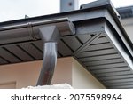 Small photo of Corner of house with new gray metal tile roof and rain gutter. Metallic guttering system, guttering and drainage pipe exterior
