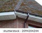 Small photo of Corner of house with old roof from bituminous tile with moss and rain gutter. Metallic Guttering System, Guttering and Drainage Pipe Exterior