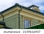 Small photo of Corner of house with windows, new green metal tile roof and rain gutter. Metallic Guttering System, Guttering and Drainage Pipe Exterior