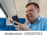 Small photo of Disgusted and overwhelmed man stares at screen of smartphone with confuse, bad joke or inappropriate content. Sad millennial guy looks at phone screen in surprise, sits in commuter train.