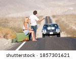 Side view Wide shot of a young couple on vacation hitchhiking on a desert road