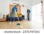 Small photo of Two Asian young professional cleaning service women worker team working in the house. Girls housekeeper sweeps broomsticks on the wooden floor with another one cleaning under the sofa. Cleaner.