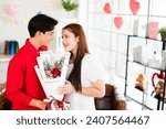 Small photo of A young Asian man surprised his girlfriend by giving her a rose and flower bouquet for her anniversary date at home. Asian woman enjoy receiving bouquet from her boyfriend. Valentine's Day celebration