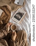 Small photo of A girl holding a cup or coffee and reading a book from “Between A Wolf and A Dog by Georgia Blain” on bed and from black books by penguin classics. Kediri, Indonesia - 07 September 2023. aesthetic