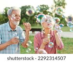 Small photo of Happy active senior couple having fun blowing soap bubbles in park outdoors. Vitality and active senior couple concept