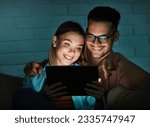 Portrait of young happy couple using tablet computer at night, using modern technology having fun with glowing screen in dark office or at home, watching tv together at home. Shot of a couple resting 