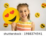 World emoji day. Anthropomorphic smile Face. Birthday Party. Emotions. A little girl, smiling with all her teeth, holds a cardboard love emoji in her hands. World Happiness day
