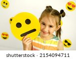 Small photo of A cute beautiful smiling girl holds a cartoon cardboard sad face smile. A variety of emotions. Different Temperament: Sanguine choleric melancholic phlegmatic