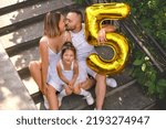 Small photo of A squeamish Girl makes a face in response to a kiss from her parents. The child's fifth birthday. Funny family celebrates daughter's first anniversary