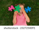 Small photo of A ludicrous child is playing with puzzles while lying on the lawn grass. Children's toys for the development of logic and thinking