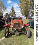 Small photo of Chascomus, Argentina - Apr 15, 2023: Old red 1915 Ford Model T open runabout roadster on the lawn. Front view. Nature, green, grass and trees. Classic car show.