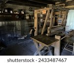 Small photo of Mitchell, Indiana, USA - June 20, 2022: Fireplace, table and weaver’s loom inside an 1800’s weaver’s shop in the recreated and restored Pioneer Village at Spring Mill State Park, near Mitchell, India