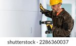 Small photo of Construction work banner. The worker using aku screwdriver for preparing hole to the mineral insulation board for insulation fastener.