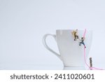 Climber climbing with rope on a white coffee cup, white background, miniature figures scene
​