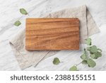 Wooden board on linen napkin on marble kitchen table withgreen leaf, flatlay