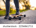 Woman rides at straight road on longboard at sunset time. Skater in casual wear training on board during evening sunset with orange light. Girl hold longboard in hands