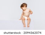 Shy happy child. Portrait of little cute toddler boy, baby in diaper calmly sitting and laughing isolated over white studio background. Concept of childhood, motherhood, life, birth. Copy space for ad