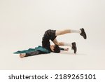 Portrait of stylish young man in black outfit and green coat posing, lying on floor isolated over grey background. Weirdness. Concept of modern fashion, art photography, style, queer, uniqueness, ad