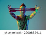 One young rhythmic gymnast posing with clubs in front of her face isolated on gradient green background in neon light. Concept of action, motion, sport life, motivation, competition. Copyspace for ad