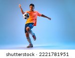Small photo of Portrait of young man, football player in motion, action, kicking ball with knee isolated over blue background in neon light. Concept of sport, team game, action, motion. Copy space for ad, poster