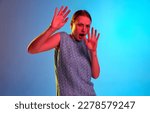 Small photo of Antipathy, dislike. Scared young girl with grimacing face and disgusted gestures over blue background in neon light. Concept of youth, human emotion, self expression, mood, ad
