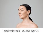 Small photo of Profile photo smiling beautiful mature woman with bare shoulders looking away over grey background. Model with well-kept skin. Fashion, beauty, spa, cosmetology, skin care concept.