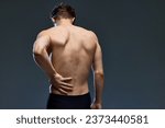 Rear view portrait of young brunette man posing, holding his muscular, healthy back isolated over dark grey studio background. Concept of men's health, beauty, fashion, wellness. Copy space. ad