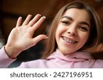 Small photo of Young attractive positive woman in fashion pink hoodie waving hallo while looking at camera against blurred background. Concept of beauty care and medicine, leisure time, style. Ad
