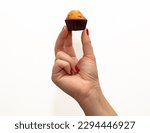 Close-up of a woman's hand with red fingernails holding a mini chocolate chip cupcake on a white background.