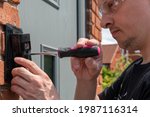 Man installing a smart doorbell with security camera and solar charger next to the front door of his house