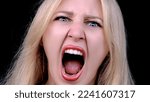 Small photo of Angry woman yells in rage as she looking at camera on black background. Headshot of girl screaming into camera with her mouth open. Resentment, discontent, hatred.