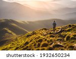 Girl on mountain peak with green grass looking at beautiful mountain valley in fog at sunset in summer. Landscape with young woman on the trail, foggy hills, forest, sky. Travel and tourism. Hiking	