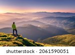 Small photo of Sporty man on the mountain peak looking on mountain valley with sunbeams at colorful sunset in autumn in Europe. Landscape with traveler, foggy hills, forest in fall, amazing sky and sunlight in fall