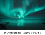 Aurora borealis over the sea. Northern lights in Lofoten islands, Norway. Starry sky with polar lights. Night landscape with aurora, sea with blurred water and sky reflection, sandy beach. Aurora 