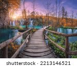 Small photo of Waterfall and wooden path in orange forest in Plitvice Lakes, Croatia at sunset in autumn. Colorful landscape with trail in park, trees, water lilies, river, pink sky in fall. Trail in woods. Nature