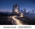 Flashlight trails on mountain path against high rocks at night in spring. Dolomites, Italy. Colorful landscape with light trails, trail on the hill, mountain peaks, purple sky with stars in summer