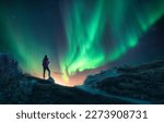 Northern lights and young woman on mountain peak at night. Aurora borealis and silhouette of alone girl on mountain trail. Landscape with polar lights. Starry sky with bright aurora. Travel background