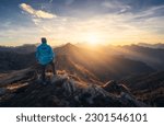 Man on stone on the hill and beautiful mountain valley in haze at colorful sunset in autumn. Dolomites, Italy. Guy, mountain ridges in fog, orange grass and trees, blue sky with sun in fall. Hiking	