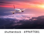 Passenger airplane. Landscape with big white airplane is flying in the red sky over the clouds and sea at colorful sunset. Passenger aircraft is landing at dusk. Business trip. Commercial plane.Travel