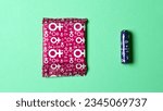 Small photo of A sanitary napkin and a tampon lie on a green background. View from above. Gasket in red packaging. A tampon in a lilac package. Horizontal image. Flatley