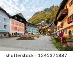 Autumn scenery of the old town square of Hallstatt, with a statue in the center, traditional colorful houses around the paved square & fall mountains in background in Salzkammergut region of Austria