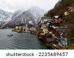 Scenery of Hallstatt on a cold winter morning, with a tourist ferry boat on the lake, a church tower among old houses in the village and snow dusted mountains in background, in Salzkammergut, Austria